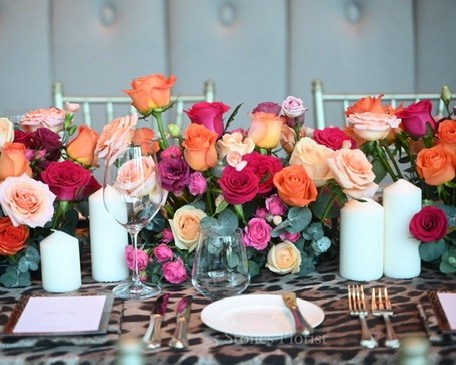 Detailed view of dark pink, orange and peach roses, eustomas, and mixed foliage in a vibrant floral table garland