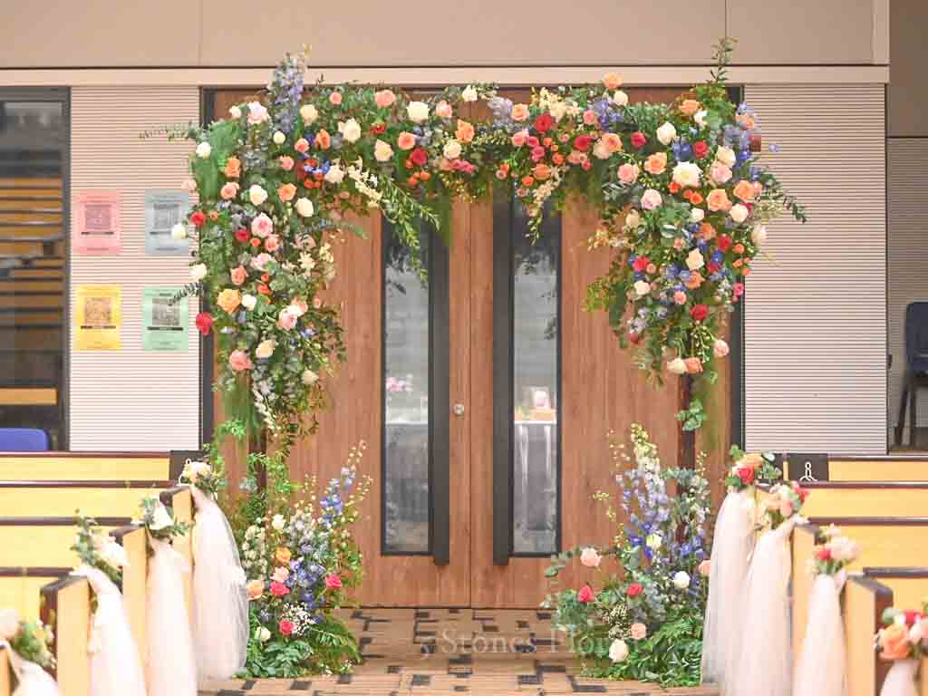 Colourful spring wedding floral arch at Grace Baptist Church entrance by 5 Stones Florist